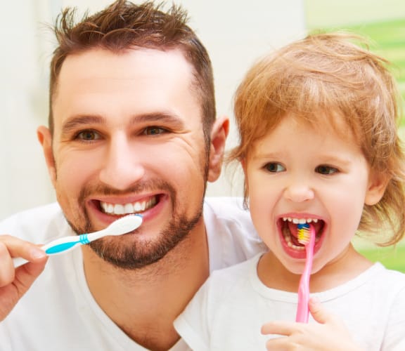 Father and daughter in front of the mirror brushing their teeth